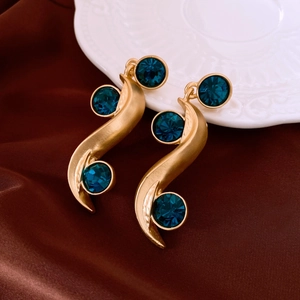 Detailed view of S-shaped golden earrings with three inset blue gems on silk background