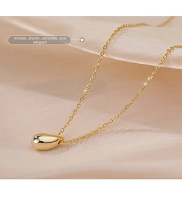 Macro shot of gold teardrop pendant necklace on elegant champagne silk background