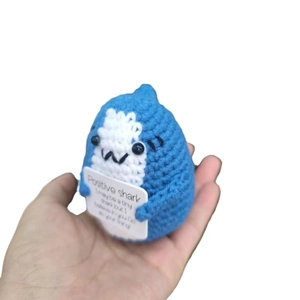 Handgefertigte gehäkelte blaue Hai-Puppe mit Motivationskarte auf weißem Hintergrund