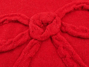 Macro shot of red knitwear showing intricate cable texture and a large 3D knitted bow detail