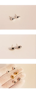 Polished gold and silver oval bean stud earrings displayed on a hand and beige surface