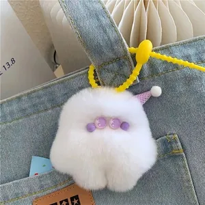 Detail of cute white plush monster keychain with purple party hat on a denim bag