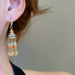 Detail shot of bohemian gold earrings with colorful beads and leaf pendants on model