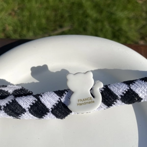 Détail de la pince à cheveux à carreaux avec pendentif chat blanc et texte doré élégant