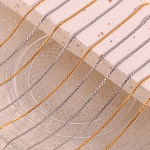 Detailed macro view of 18K gold and silver stainless steel snake chains on stone surface