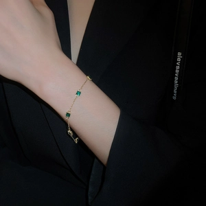 Détail d'un bracelet plaqué or avec des pierres vert émeraude carrées sur un poignet