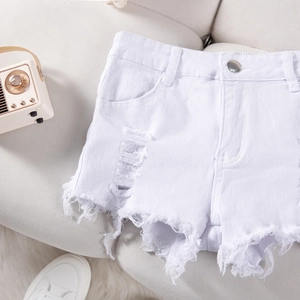 Detail view of white distressed denim shorts with ripped edges on a soft beige sofa