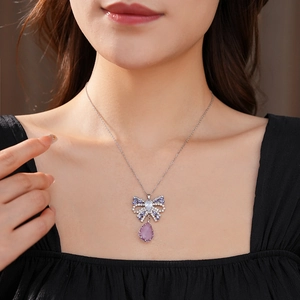 Detail of silver bow pendant with purple teardrop gemstone worn by a model