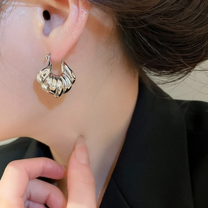 Close-up of silver croissant shell earrings with metallic texture on a female model