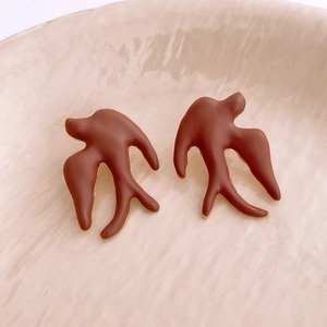 Detail of brown swallow-shaped matte earrings on a water-textured ceramic tray