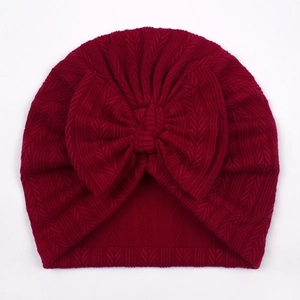 Macro detail of dark burgundy knitted baby turban hat with a large bow and herringbone texture