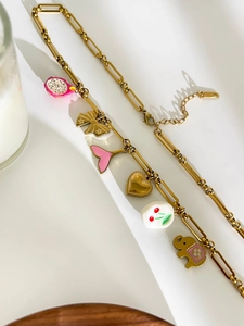 Detail of a golden paperclip chain necklace with colorful enamel charms like a pink fish tail