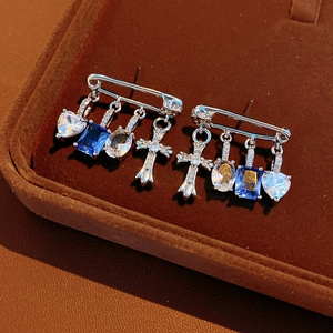 Close-up of silver safety pin earrings with blue zircon heart and cross charms