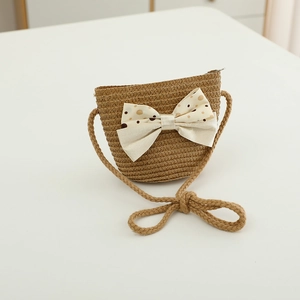 Detail view of a straw crossbody bag for children with a cream polka dot bow decoration
