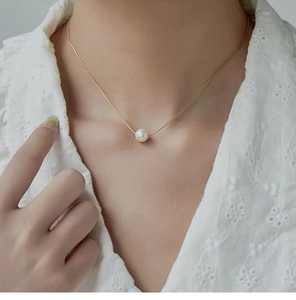 Close-up of minimalist gold titanium steel necklace with a single round white pearl