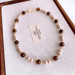 Vintage tiger eye stone and pearl beaded necklace with gold zircon clasp on wooden tray