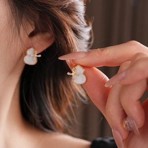 Macro detail of gourd stud earrings with gold plating, mother of pearl and bow accents