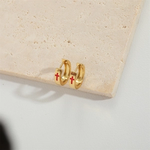 Minimalist gold hoop earrings with red cross design on a neutral stone background