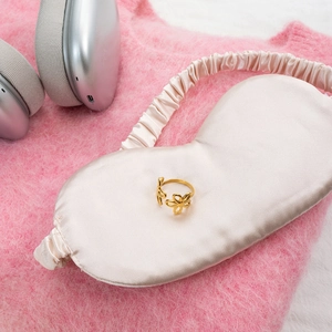 Detailed close-up of an 18K gold hollow flower ring placed on a soft silk eye mask