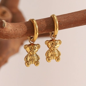 Detailed close-up of 18K gold plated teddy bear charm hoop earrings on a wooden branch
