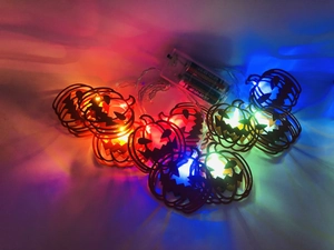 Detail of colorful LED Halloween pumpkin string lights with battery pack on white background