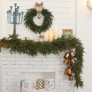 Christmas pine cone wreath and garland with burlap bows and bells on a fireplace mantle
