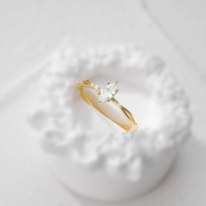 Dettaglio macro di un anello con diamante marquise e fascia d'oro intrecciata su bianco