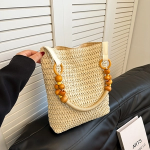 Beige straw woven handbag with wooden bead accents and hemp rope handles on casual sofa