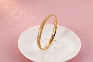 Close-up of golden titanium steel bangle with frosted finish on a white ceramic plate