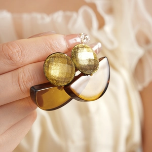 Detail view of golden glitter resin earrings held by hand in a bohemian fan style
