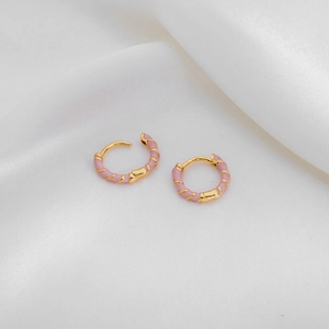 Detailed macro of pink enamel spiral pattern on golden hoop earrings for women
