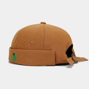 Detail of caramel canvas docker cap featuring green shamrock embroidery and metal buckle