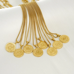 Flat lay of 18k gold zodiac coin pendants with embossed symbols on white silk fabric