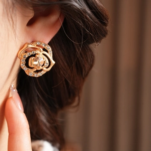 Close-up of gold rose earrings with crystals and a large gemstone on model