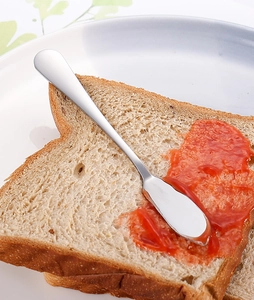Gros plan d'un couteau à beurre en inox étalant de la confiture rouge sur un toast