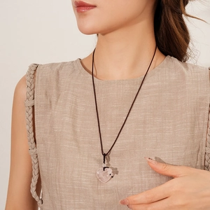 Detail view of pink heart-shaped stone pendant on brown woven rope necklace worn by model