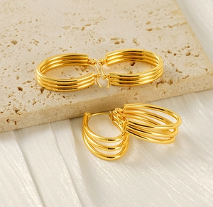 Macro detail of 18k gold plated triple layer hoop earrings on travertine and silk background