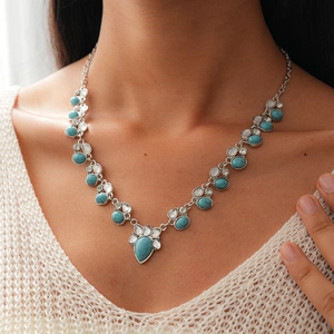 Detail of bohemian silver necklace with turquoise stones and rhinestones on white sweater