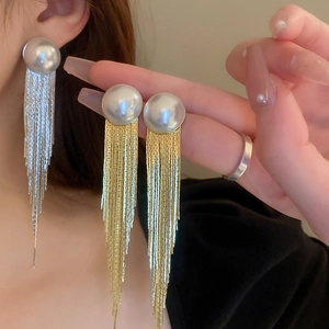 Detail of long fringe earrings with large pearls and metallic chains on a model