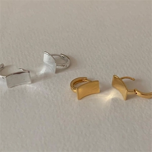 Detail of curved brushed silver and gold hoop earrings on a textured background