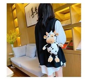 Rear view of a plush cow-shaped backpack with black and white spots worn by a model
