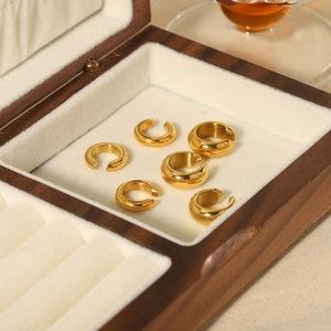 Macro view of six gold-plated C-shaped ear cuffs displayed in a wooden velvet jewelry box