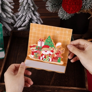 Detail showing hand holding a 3D pop-up Christmas card with Santa and reindeer on wood tray