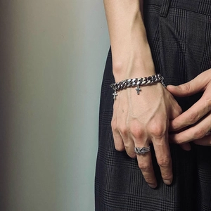 Detail view of silver Cuban link chain bracelet with crosses and woven texture ring