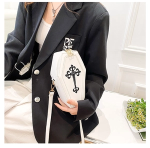 Detail of a white coffin-shaped crossbody bag with black gothic cross on a black blazer