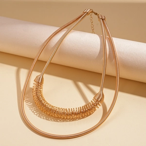 Détail d'un collier pull doré à double couche avec ressort sur un support minimaliste