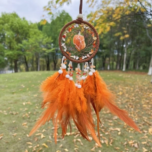 Detail of dream catcher with orange feathers and natural stones against a blurred background
