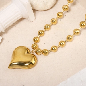 Detailed view of the 18K gold heart pendant on a chunky ball chain against a neutral background