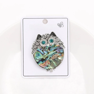Detail of owl brooch with abalone shell belly and green rhinestone eyes on display card