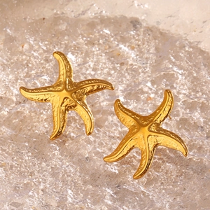 Golden starfish stud earrings with textured finish on a sparkling summer beach water background
